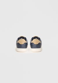 Baskets en cuir bleu marine avec accents beige clair, semelle en caoutchouc blanche, col rembourré et deux lignes de couture le long du talon.