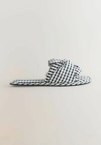 Butas be užsegimo šlepetė su juodai balta languota audinio medžiaga ir paminkštintomis kryžminėmis dirželėmis ant vientisos spalvos fono.