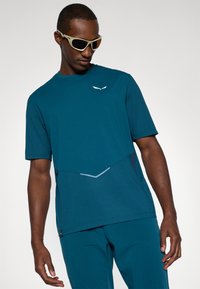 Τεαλλί μπλουζάκι αθλητικής ένδυσης με κοντά μανίκια, ριμπέ ύφανση, γεωμετρικά στοιχεία σχεδίασης και διακριτική σήμανση σε λευκό χρώμα.