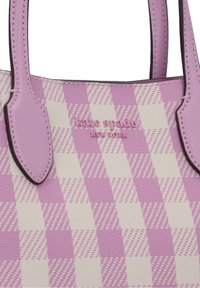 Lila- und cremefarbener karierten Handtasche mit strukturiertem Oberflächen, ausgestattet mit pinkfarbener Logoschrift und passenden Griffen.