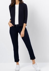 Námořnická zkrácená bunda přes bílý top, doplněná tmavě modrými džíny a bílými teniskami. Outfitem se vyznačuje štíhlým, přiléhavým střihem a ohrnutými manžetami.