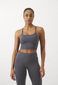 Pilkas grioveliais sportinis crop top su reguliuojamomis petnešomis, derinamas su aukšto liemens suderinamomis leggings. Lygus paviršius ir prigludęs dizainas.