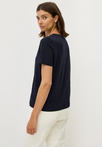 Marinblå kortärmad t-shirt i lätt material med avslappnad passform, rundad halsringning och slät textur, kombinerad med vita byxor.