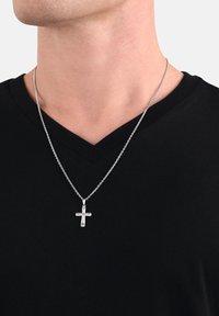 Primo piano di una persona che indossa una collana con pendente a croce d'argento sopra una maglietta nera a V.