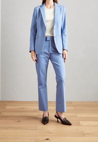 Svetle modrý blazer s odpovídajícími kalhotami, přiléhavý střih, s dvoucestným zapínáním a klopami. V kombinaci s černými slingback podpatky.