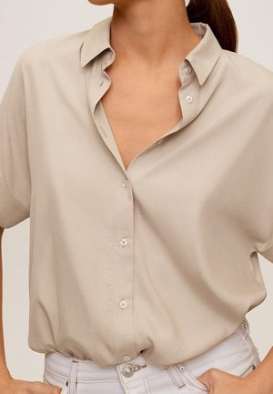 Chemise beige à manches courtes, coupe décontractée, col et patte de boutonnage. Tissu lisse avec un léger éclat, sans motifs ni accents visibles.
