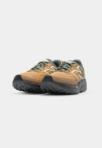 Scarpe da trail running con tomaia marrone e verde, caratterizzate da un design in mesh testurizzato e una suola in gomma nera con un motivo a tasselli.