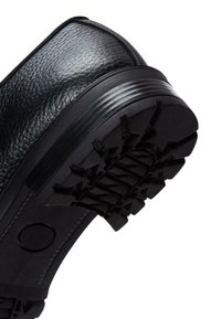Zapato de cuero negro con un upper texturizado, que presenta una suela de goma gruesa y resistente con un patrón de banda de rodadura moldeado para tracción.