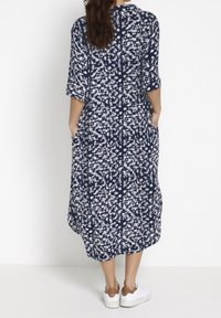 Námořnicky modré květinové šaty s volným střihem, rukávy po lokty a kapsami. Bílé květinové vzory po celém povrchu, kombinované s bílými teniskami.