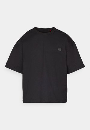 Black oversized short-sleeve t-shirt with crew neck and small square patch on the left chest, displayed on a light grey background.