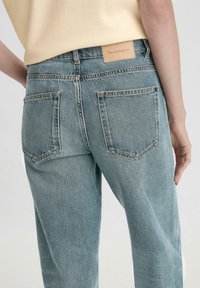 Jeans in denim blu chiaro con vita alta, taglio dritto e tasche posteriori visibili. Etichetta di stoffa sulla cintura con il logo "hessnatur" impresso.