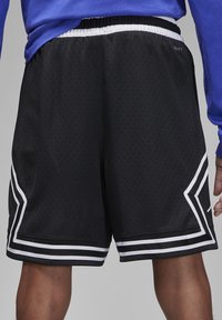 Black athletic shorts made of perforated fabric, featuring white stripes along the sides and hem. Elastic waistband for comfort.