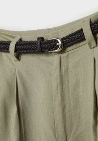 Khaki linnen broeken met diepe plooien, voorzien van een zwarte gevlochten riem en zilveren gesp, die de textuur en kleurcontrasten benadrukken.