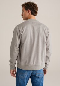 Hall hall puuvillane dressipluus soonikkoelise krae, pikkade varrukate ja lõdva istuvusega, kombineeritud siniste teksadega. Tekstuur näib olevan sile.