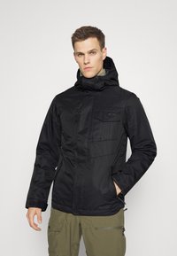 Giacca nera isolante con colletto alto, zip frontale, multiple tasche e cappuccio regolabile. Texture liscia con finitura opaca.