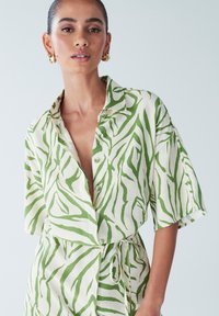 Grøn og hvid kortærmet skjorte med knapper foran, der har et zebrastribet mønster og et bånd i taljen til justerbar pasform.