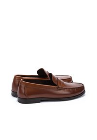 Mocasines de cuero marrón con un acabado suave, punta redondeada, detalles cosidos y una suela negra de bajo perfil. Diseño clásico tipo slip-on.