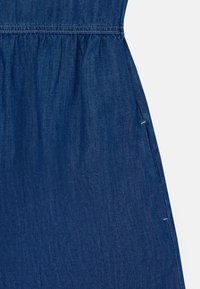 Mørkeblå denimkjole med samlet liv, med en glatt tekstur og subtil falming. Sidelommene er synlige.