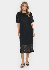 Black lace dress with short sleeves, geometric pattern, mid-calf length, featuring a sheer hem. Paired with leopard print shoes.