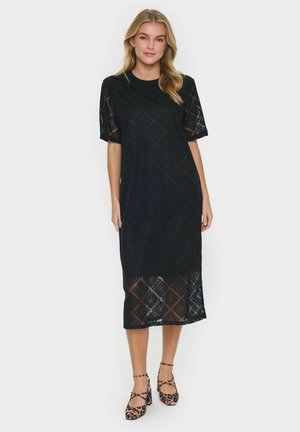 Black lace dress with short sleeves, geometric pattern, mid-calf length, featuring a sheer hem. Paired with leopard print shoes.