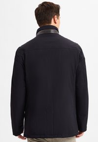 Schwarze Außenjacke mit Stehkragen und subtilen Lederdetails. Schlichtes Material, lange Ärmel und gerader Schnitt.