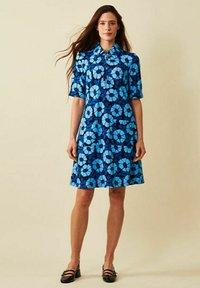 Kortärmad klänning i blått tyg med blommönster i olika nyanser av blått, med krage och en knappslå framtill.