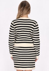 Conjunto de suéter y falda de punto en negro y crema con rayas horizontales. Presenta una textura acanalada y una silueta ajustada.