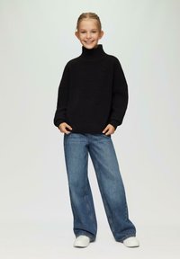 Zwarte gebreide coltrui met ribbelstructuur, gecombineerd met ruime blauwe jeans en witte sneakers. Eenvoudige en casual outfit.