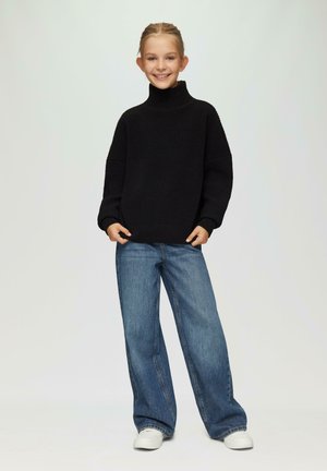 Schwarzer gestrickter Rollkragenpullover mit geripptem Material, kombiniert mit weit geschnittenen blauen Jeans und weißen Sneakers. Einfaches und lässiges Outfit.