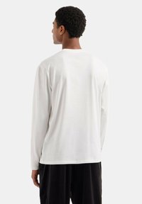 Camicia bianca di cotone a maniche lunghe con collo tondo. Tessuto morbido e vestibilità comoda, abbinata a pantaloni neri.