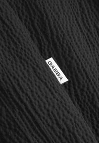 Material textil negru cu un model textured și un eticheta albă mică pe care scrie "GABBA" atașată de acesta.