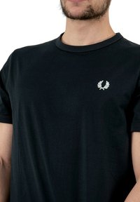 T-shirt in cotone nero con collo rotondo e maniche corte, decorato con un piccolo emblema ricamato bianco sul lato sinistro del petto.
