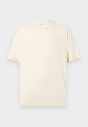 Lihtne lühikeste varrukatega beež T-särk ümara kaelusega, esitatuna lamedana helehalli tausta peal.