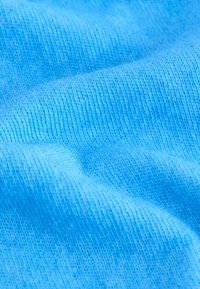 Light blue knit fabric with fine texture and visible stitching patterns, showing smooth curves and soft draping.