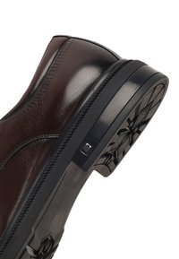 Bruine leren enkellaars met een glanzende afwerking en gestructureerde details. Heeft een zwarte rubberen zool met een patroon en een zijaccent.