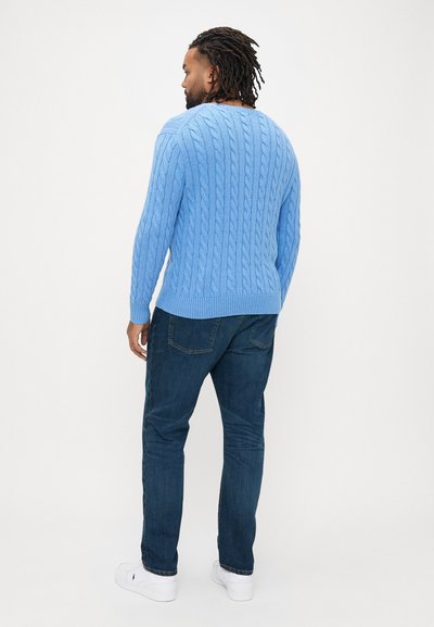 Πλεκτό πουλόβερ με σχέδιο καλωδίου σε ανοιχτό γαλάζιο χρώμα, με μακριά μανίκια και στρογγυλή λαιμόκοψη. Συνδυάζεται με σκούρο μπλε τζιν και λευκά αθλητικά παπούτσια.