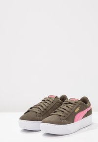Zamszowe trampki w kolorze oliwkowym z różowymi akcentami, zaokrąglonym noskiem, białą gumową podeszwą i wiązaniem na sznurowadła. Posiadają logo Puma po bokach i na języku.