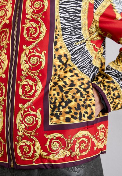 Röd jacka med guld-accenter som har djurmönster – leopard och zebra – med dragkedja och elastiska ärmslut.
