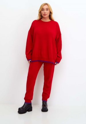 Czerwona, oversize'owa bluza z okrągłym dekoltem, zestawiona z pasującymi czerwonymi joggerami. Fioletowe wykończenia przy mankietach i hemie. Czarne platformy.