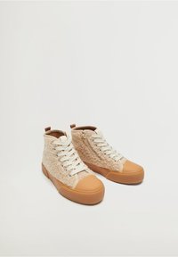 Vysoké tenisky s béžovým texturovaným textilním svrškem, hnědou gumovou špičkou a podešví, krémovými tkaničkami a bočním zipem pro snadné oblékání.