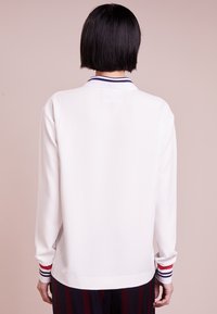 Camicia bianca a maniche lunghe con colletto a contrasto caratterizzato da strisce navy, rosse e bianche. Tessuto liscio e vestibilità comoda, con polsini a costine.