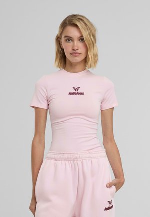 Lys rosa tettskjorte med korte ermer, med en mørkere rosa logo "felicitous" på brystet. Glatt bomullslignende tekstur.