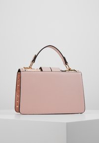 Rosa läderhandväska med en strukturerad design, guldiga detaljer och dekorativa nitar längs sidan. Har ett handtag upptill och en låsning.