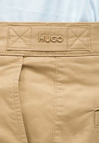 Ζώνη παντελονιού σε μπεζ χρώμα με κεντημένο λογότυπο "HUGO" και λεπτομερείς ραφές και ενισχυμένο ράψιμο στις περιοχές με υφασμάτινες θηλιές.