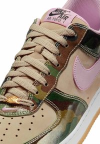 Nike Air Force 1 sneakers med beige ruskind, camouflage-detaljer, pink Swoosh og en guld tag. Teksturerede snørebånd og perforeret tåboks.