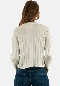 Maglione grigio chiaro a coste con maniche lunghe, in un tessuto a maglia testurizzato e una vestibilità comoda, indossato sopra jeans blu scuro.