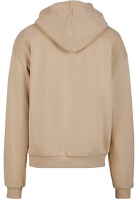 Beige kapucnis pulóver laza szabással, bordázott mandzsettákkal és szegéllyel. Simább textúra, minimalista dizájn, látható logók vagy akcentusok nélkül.