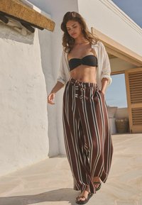 Smešane smeđe i bijele pruge široke pantalone sa džepovima, uparene s crnim bandeau topom i laganom bijelom košuljom koja se nosi otvorena. Crne sandale.