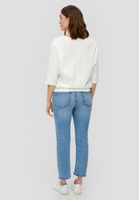 Weißes, strukturiertes Oberteil mit 3/4-Ärmeln, kombiniert mit hellblauen, knöchellangen Jeans. Weiße Sneakers runden das Outfit ab. Einfaches, lässiges Design.
