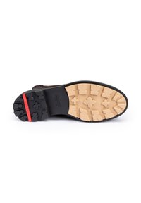 Suola della scarpa caratterizzata da un bordo in gomma nera, un battistrada beige con schemi di grip pronunciati e una sottile striscia rossa. Design robusto e testurizzato.